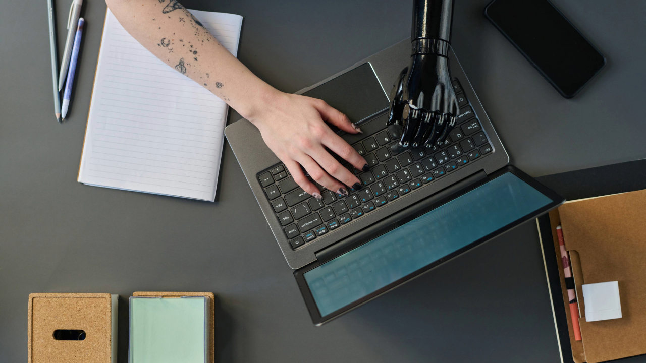 Human hand and robotic AI hand collaborating Human hand and robotic AI hand collaborating together on a laptop keyboard, symbolizing human-AI partnership in modern technology and future work